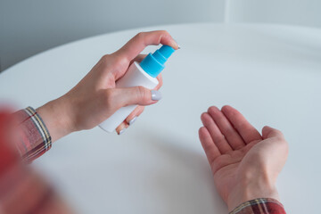 Woman spraying antiseptic on hands - close up, selective focus, over shoulder view. Spray disinfection, protection, prevention, COVID-19, coronavirus, safety, sanitation concept
