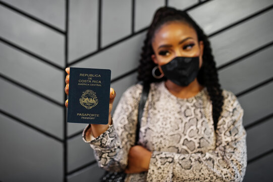African american woman wearing black face mask show Costa Rica passport in hand. Coronavirus in America country, border closure and quarantine, virus outbreak concept.