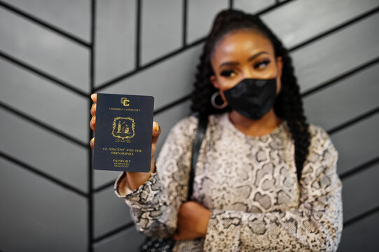 African american woman wearing black face mask show Saint Vincent and the Grenadines passport in hand. Coronavirus in America country, border closure and quarantine, virus outbreak concept.