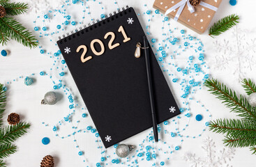 Black notepad with digits 2021 among New Year decorations on white wooden background