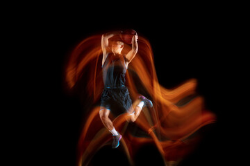 Playing on fire. Young east asian basketball player in action and motion jumping in mixed light...