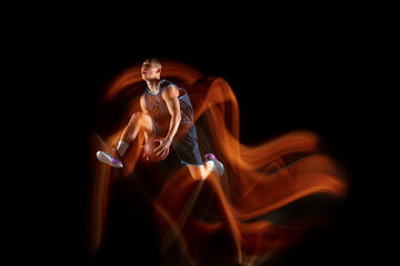 Playing on fire. Young east asian basketball player in action and motion jumping in mixed light over dark studio background. Concept of sport, movement, energy and dynamic, healthy lifestyle.