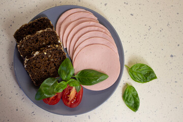 Sausages, bread, tomato, basil leaf on grey plate on light marble background, top view