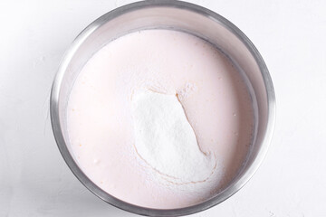 Step by step recipe of sponge cake. Step 6. Flour added into the mixture of eggs and sugar in the metallic bowl. Top view