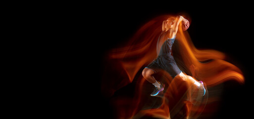 Flyer with copyspace. Young east asian basketball player in action and motion jumping in mixed light over dark studio background. Concept of sport, movement, energy and dynamic, healthy lifestyle.