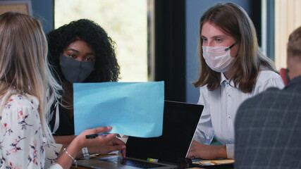 Women at workplace with COVID-19 epidemic protection. Three happy multiethnic young female colleagues work in face masks