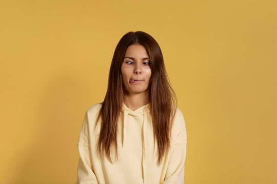 Crazy friendly caucasian woman in yellow hoodie makes funny face, crosses eyes and sticks out tongue, plays fool, doesnt want to be serious, being in good mood. Isolated over a yellow background.