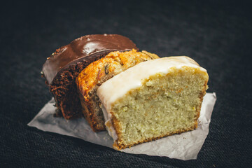 Slices of chocolate bread, banana bread, and lemon bread on rustic paper.