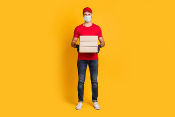 Fototapeta premium Photo of young courier guy hold pile boxes wear mask red t-shirt hat jeans footwear isolated yellow color background