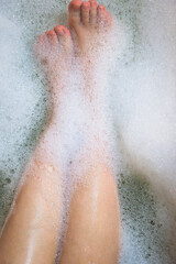 Women's legs in the bathtub, bathing with bubble bath foam top view, relaxtion beauty spa concept