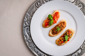 Crostini with meat sauce, tomatoes, basil and peppers on a white plate