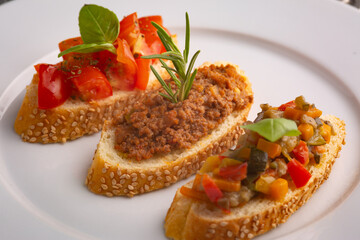 Crostini with meat sauce, tomatoes, basil and peppers on a white plate