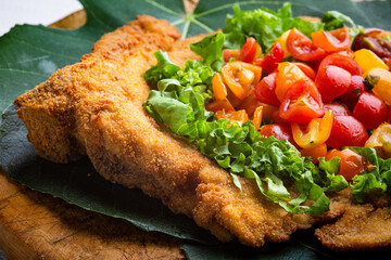 Veal milanese (cotoletta alla milanese) with fresh vegetable and tomatoes, salad close-up on a plate. horizontal top view from above
