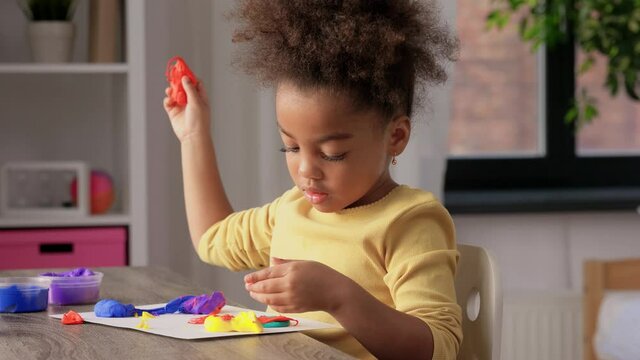 childhood, creativity and hobby concept - little african american girl with modeling clay playing at home