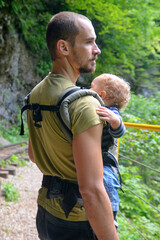 Travel with small children. Father with baby in carrier walks in mountain gorge.