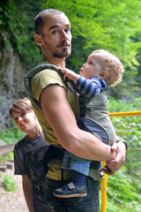 Travel with small children. Father with baby in carrier and ten year old son walking in mountain gorge.