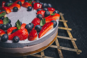 Fruit cake, based on a blueberry and strawberry mousse, with mint details, on a rustic metal grid. Totally gluten free. Dark background.