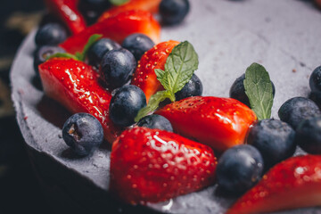 Fruit cake, based on a blueberry and strawberry mousse, with mint details, on a rustic metal grid. Totally gluten free. Dark background.