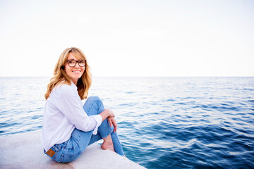 Fototapeta na wymiar Beautiful mature woman sitting on cliff and relaxing by the sea