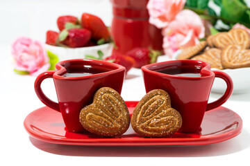 two red coffee cups and heart shaped cookies on white table, closeup