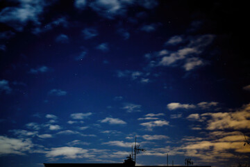 Night sky with clouds and part of the building with antenna and stars.