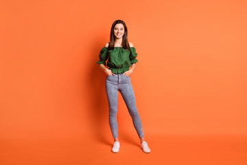 Fototapeta na wymiar Full length photo of cute shiny lady dressed green off-shoulders blouse hands arms pockets isolated orange color background