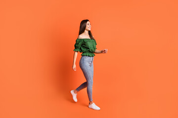 Fototapeta na wymiar Photo of cute adorable lady dressed green off-shoulders blouse walking looking empty space isolated orange color background