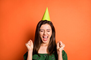 Photo of astonished lady dressed green off-shoulders blouse birthday cap open mouth rising fists isolated orange color background