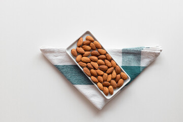 Fresh nut almonds in a ceramic bowl with a towel on a white background. Flat lay, top view, copy space.