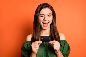 Portrait of attractive person arms hold debit banking card eye wink open mouth isolated on orange color background