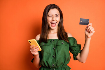 Photo of impressed girl open mouth blink hold telephone card wear dark shirt isolated on orange color background