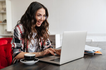 Fototapeta premium Happy nice woman smiling and working with laptop while drinking coffee