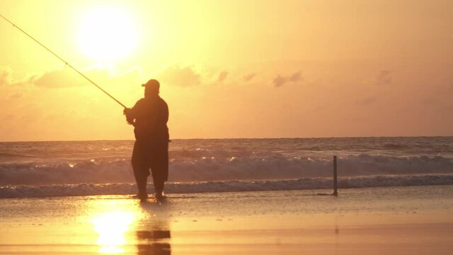 Fisherman wearing hat fishing during warm colourful sunset on the sea