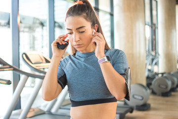 Sporty woman with wireless earbuds listening to music at gym