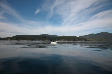 View of a fishing boat in the ocean with mountain and forest under blue sky in Vancouver Island, British Columbia, Canada