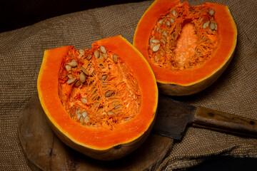 Cut ripe pumpkin. Nearby, the hatchet lies on a wooden board. Long pumpkin. Autumn vegetable.