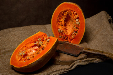 Cut ripe pumpkin. Nearby, the hatchet lies on a wooden board. Long pumpkin. Autumn vegetable.