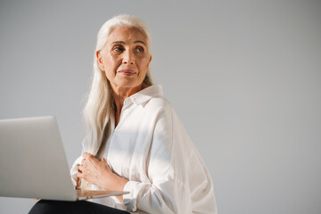 Focused elderly white-haired woman working with laptop
