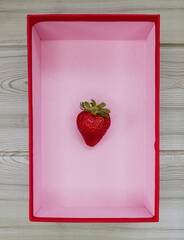 small strawberry in a red box with pink background on a beige wooden table