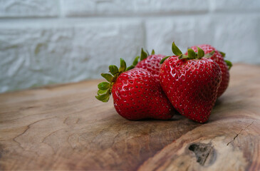 delicious fresh strawberries, a strong red on a rustic wooden table and a white brick wall background