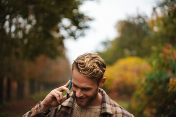 Fototapeta premium Joyful man talking on mobile phone while strolling in autumn forest