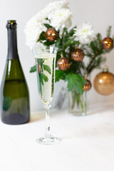 Glass of champagne, bottle, Christmas bouquet in glass vase with white chrysanthemum flowers, fir tree branch, golden balls, light garland  on white background