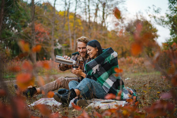 Young happy couple drinking tea and hugging while resting in forest