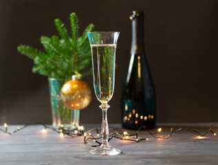 Glass with champagne and bottle on black background with christmas decoration in vase of fir tree branch, golden ball and lights garland