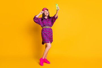 Fototapeta na wymiar Full size photo of cool funny teen girl doing selfie wear violet checkered mini dress strap pink sneakers isolated on yellow background