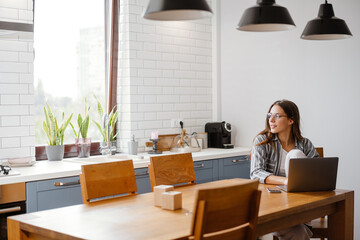 Pleased beautiful woman working with laptop while sitting at table