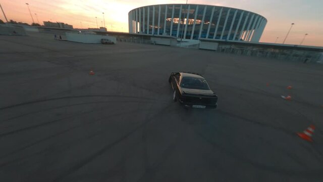 Racing black car drifting on urban square shooting from fpv drone, wheel tire tracks on asphalt road. Professional driver drifting jdm vehicle aerial follow view.