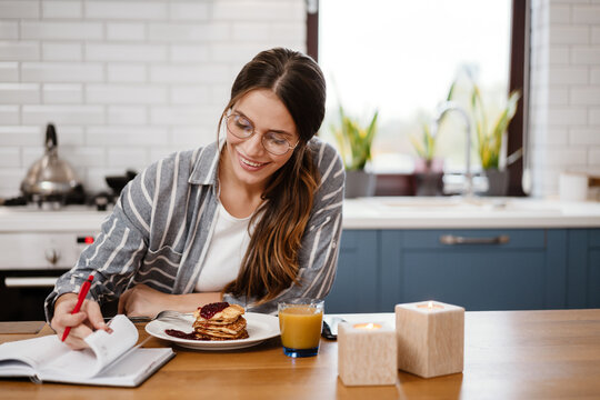 Smiling beautiful woman writing down notes while having breakfast