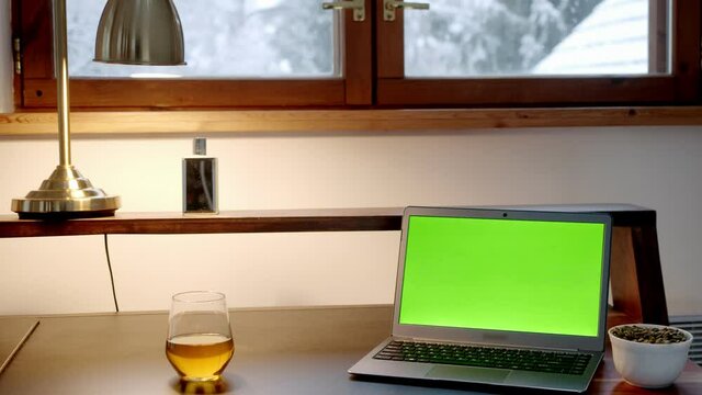 workplace in a cozy home. laptop, chromakey screen, glass of alcohol, beer or whiskey.
