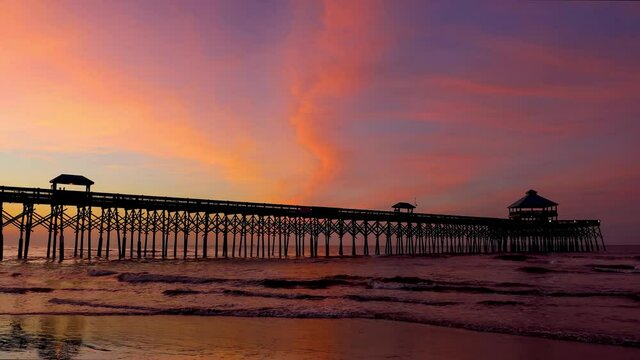 The fishing pier on island of Folly Beach, near Charleston, South Carolina, is silhouetted by a colorful sunrise sky over the Atlantic Ocean in this looping video footage.